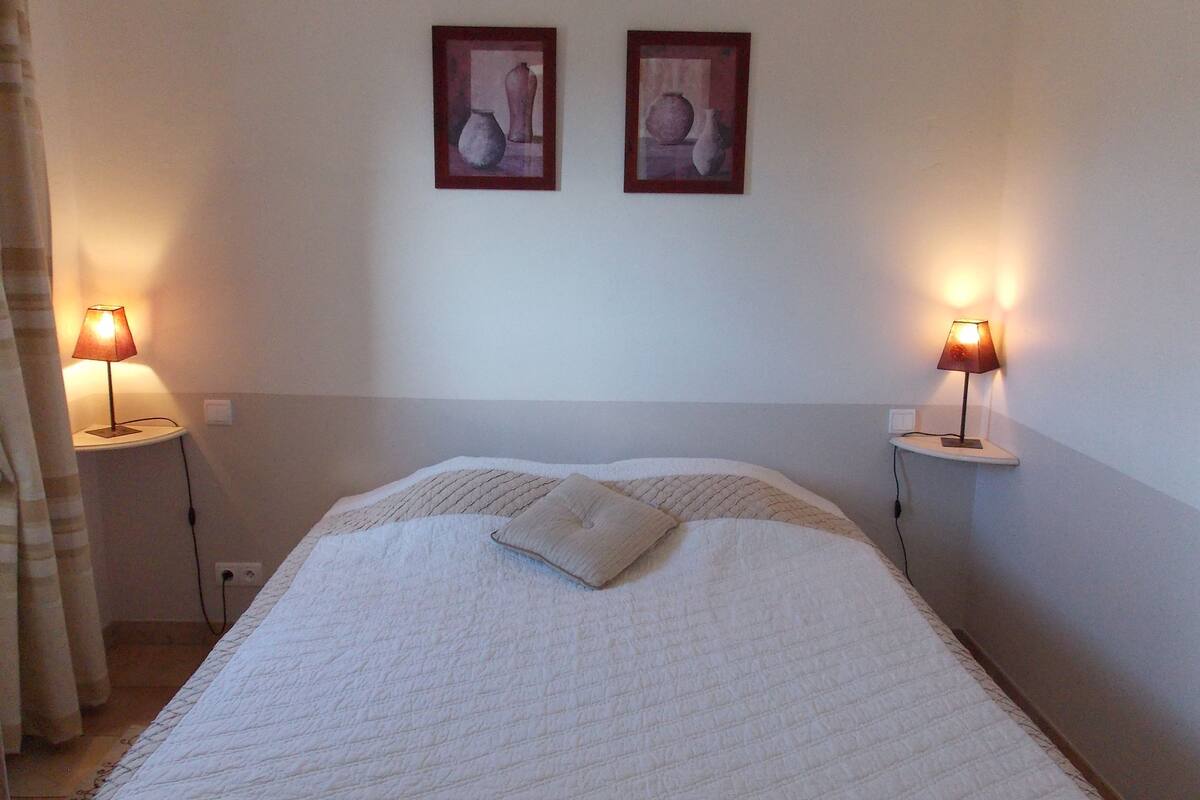 Quarto com cama, duas luminárias de cabeceira e duas fotografias emolduradas na parede.