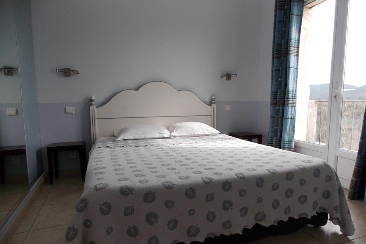 Quarto com cama, janela com cortinas e vista para o exterior.