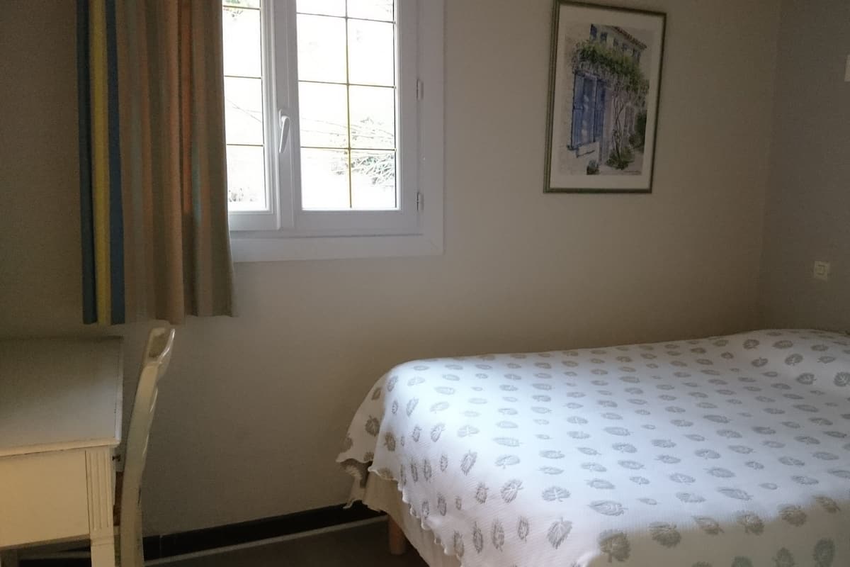 Quarto com cama, janela, cadeira e quadro na parede.