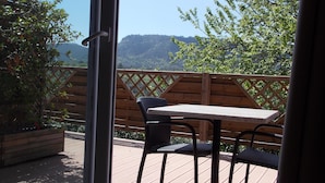 Een houten terras met een tafel en stoelen, uitkijkend op een bergachtig landschap.