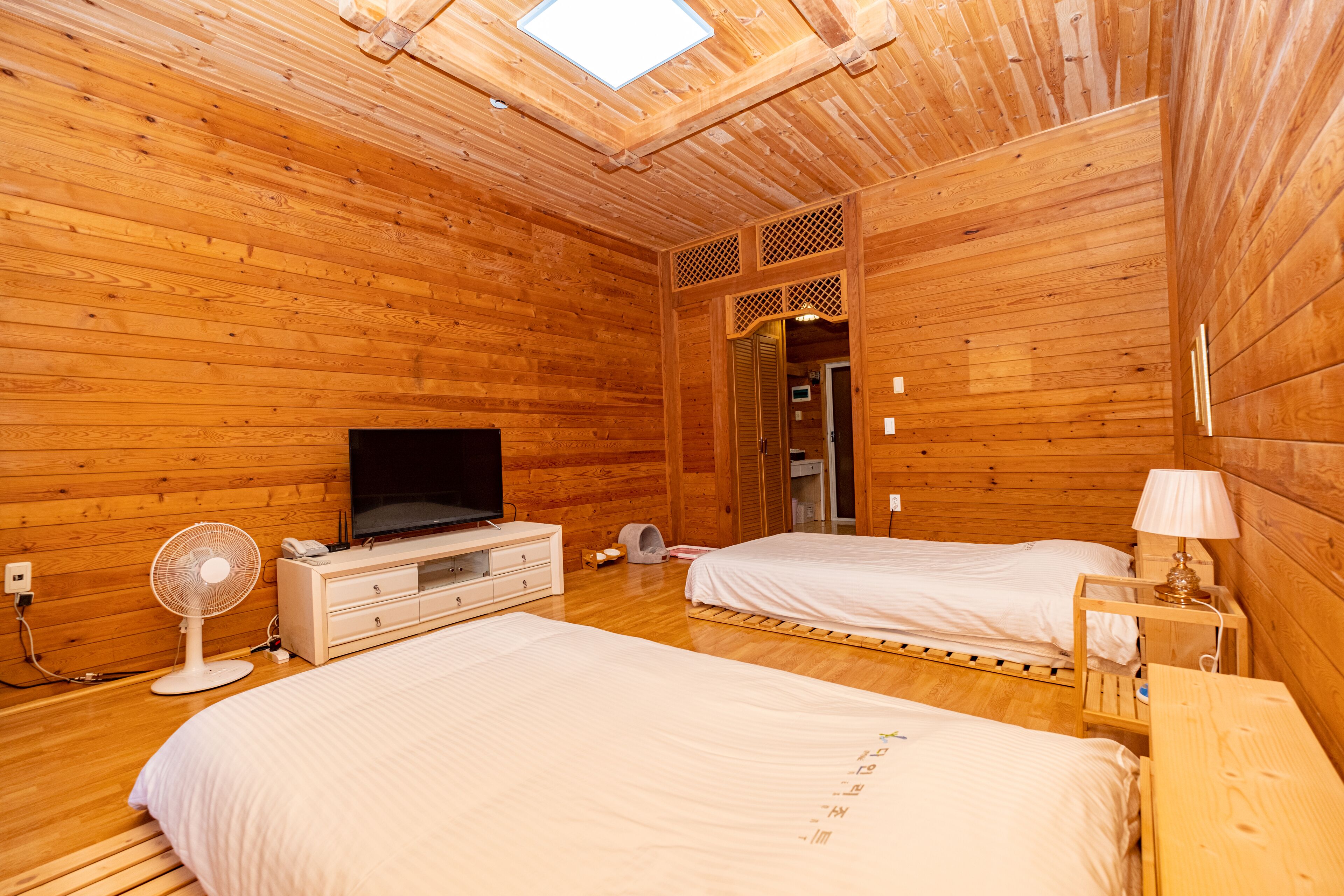 A wooden cabin-style bedroom with two beds, a TV, a fan, and a small table.