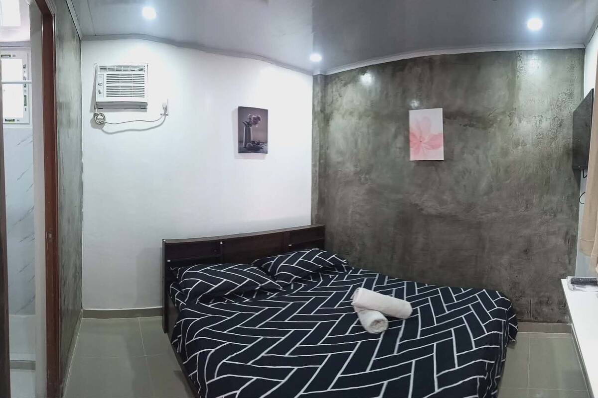 A bedroom with a bed, a wall-mounted air conditioner, and a picture frame.