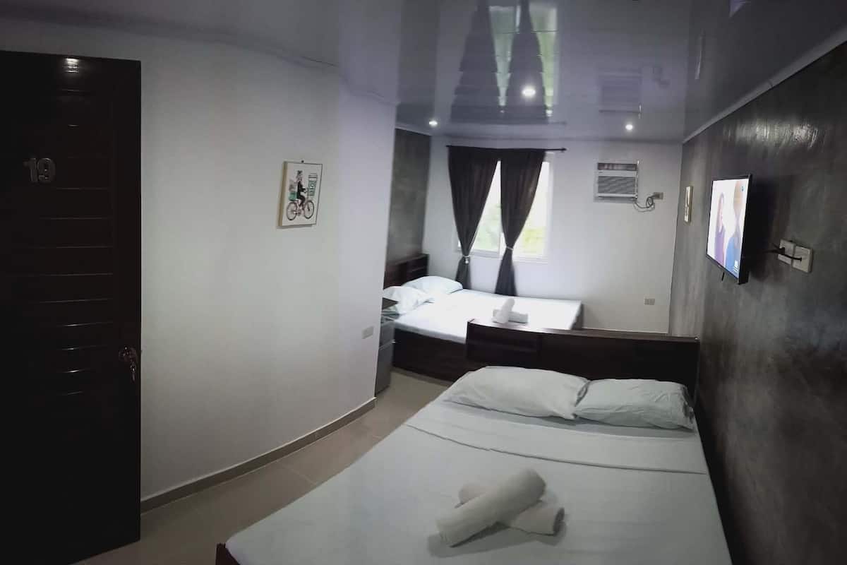 A hotel room with a bed, a desk, a chair, a TV, and a door.