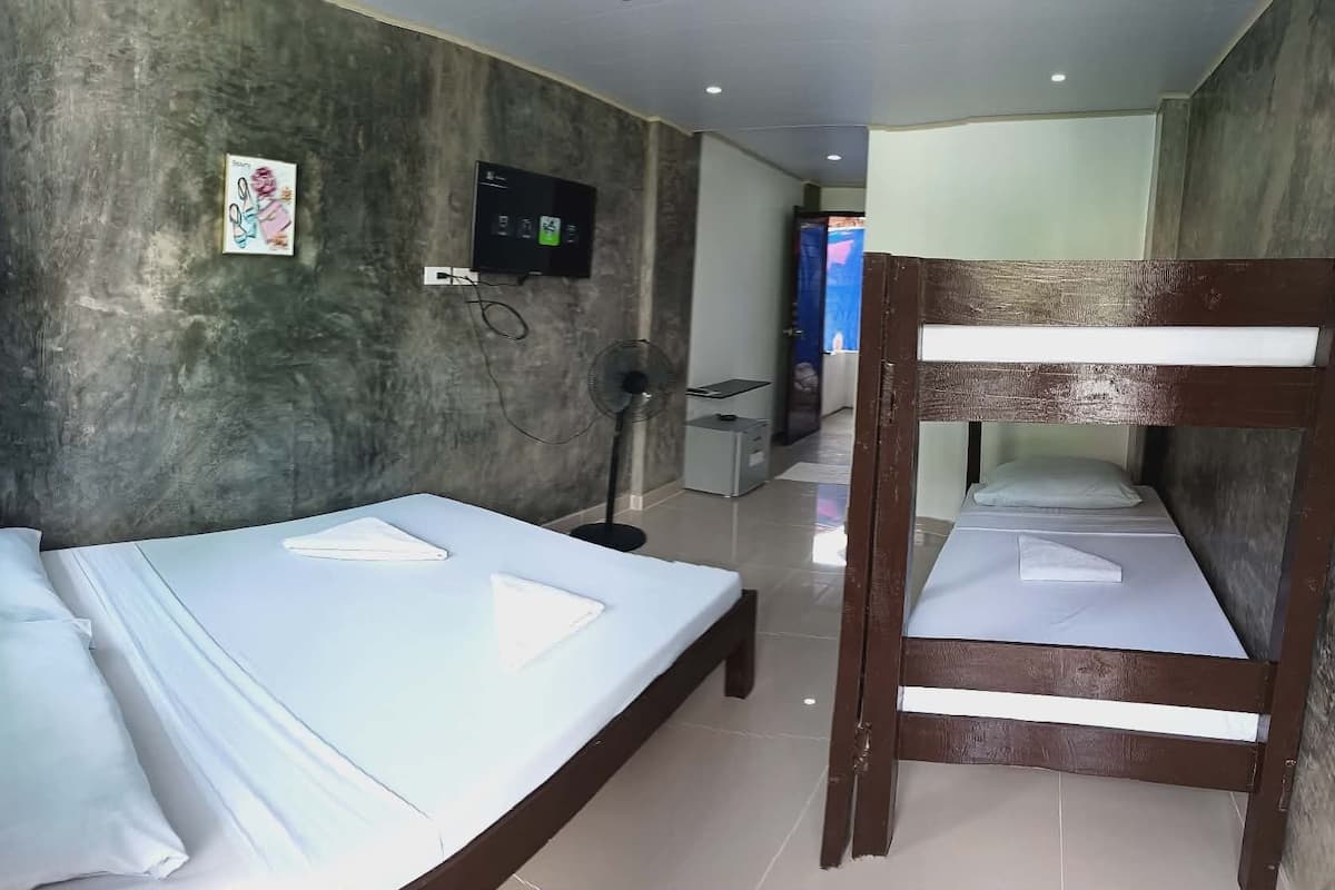 A hotel room with a bunk bed, a flat-screen TV mounted on the wall, and a small desk with a chair.