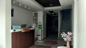 A modern reception area with a wooden counter, a small table with a vase of flowers, and a staircase leading to another level. - Lola's Lodge (Boracay Island)