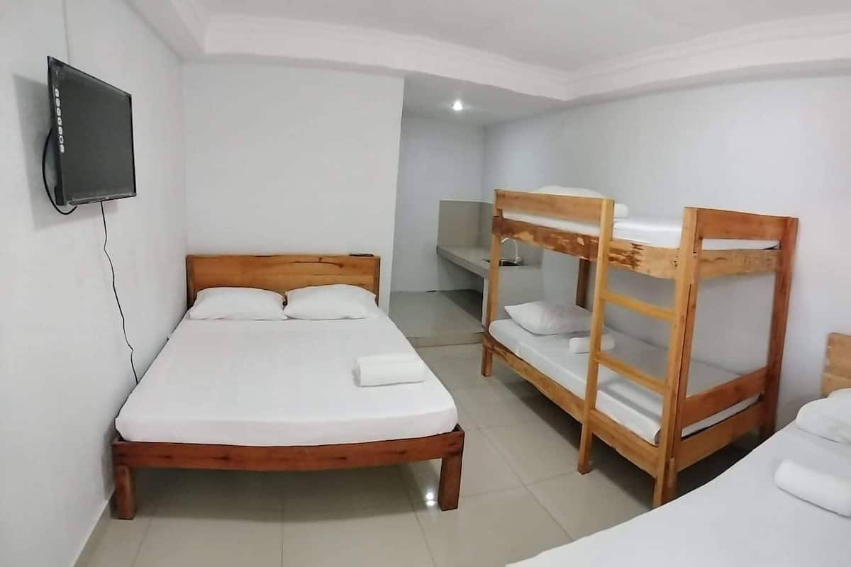 A room with a single bed, two bunk beds, a TV mounted on the wall, and a striped curtain.
