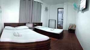 A hotel room with two beds, a wooden headboard, a small table, a chair, a TV, and a window with curtains. - Lola's Lodge (Boracay Island)