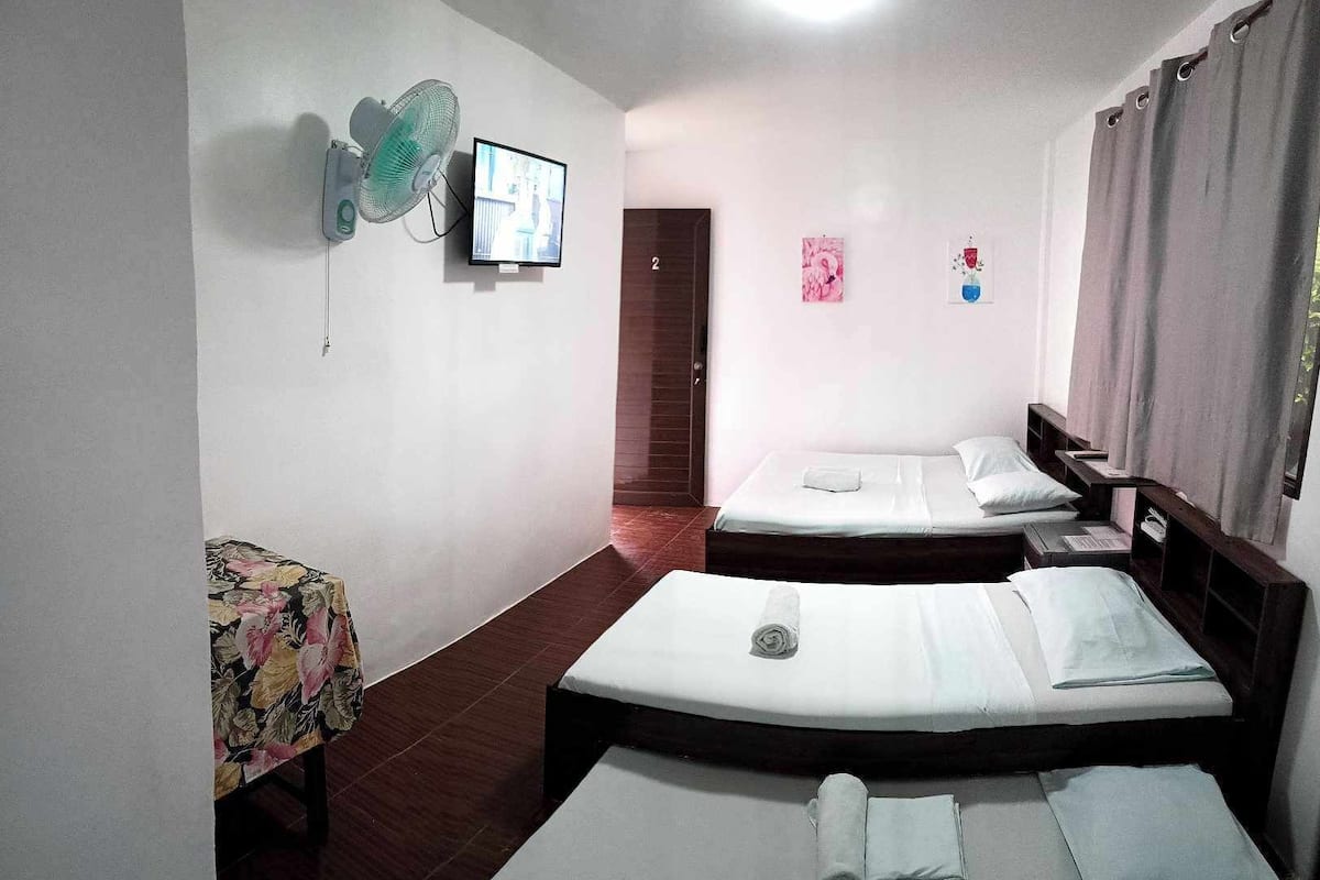 A hotel room with two beds, a TV mounted on the wall, and a small table with a floral tablecloth.