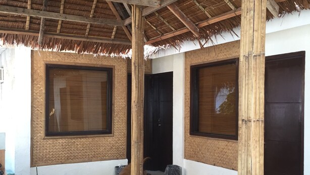 A covered outdoor area with a thatched roof, large windows, and a concrete floor. - Lola's Lodge (Boracay Island)