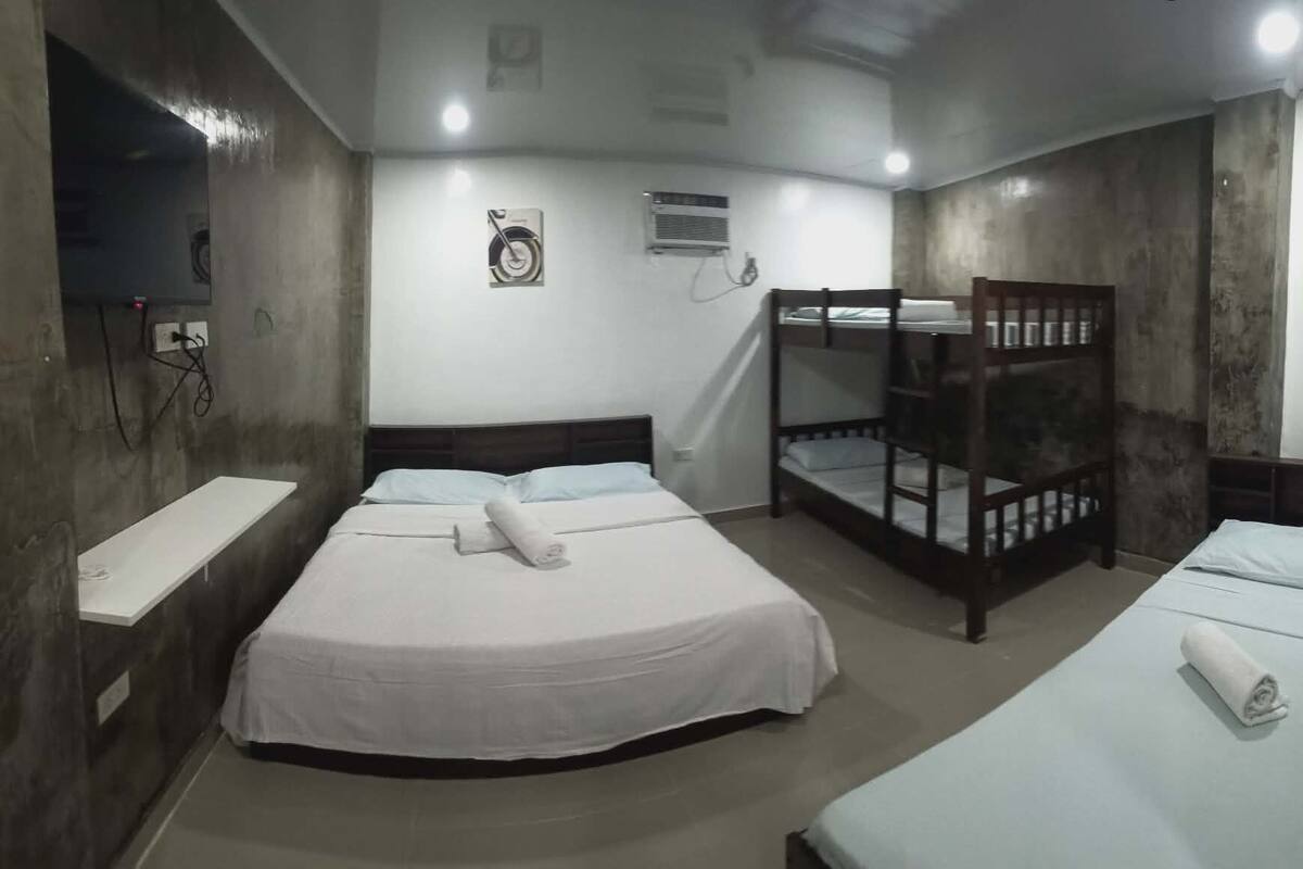 A room with bunk beds, a bedside table, a wall-mounted air conditioner, and a power outlet.