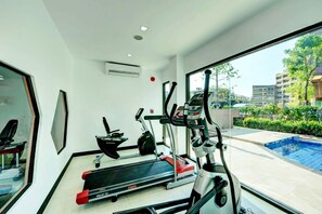 Enjoy a workout in the in-room fitness area with a treadmill, elliptical machine, and stationary bike, offering a view of the pool and surrounding greenery.