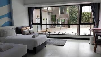 A modern hotel room with two beds, a dining area, and large windows.