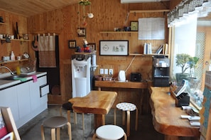 A compact kitchen with wooden walls, a sink, a refrigerator, a coffee machine, and a small dining area with stools. - Tosarang Guesthouse (Jeonju)