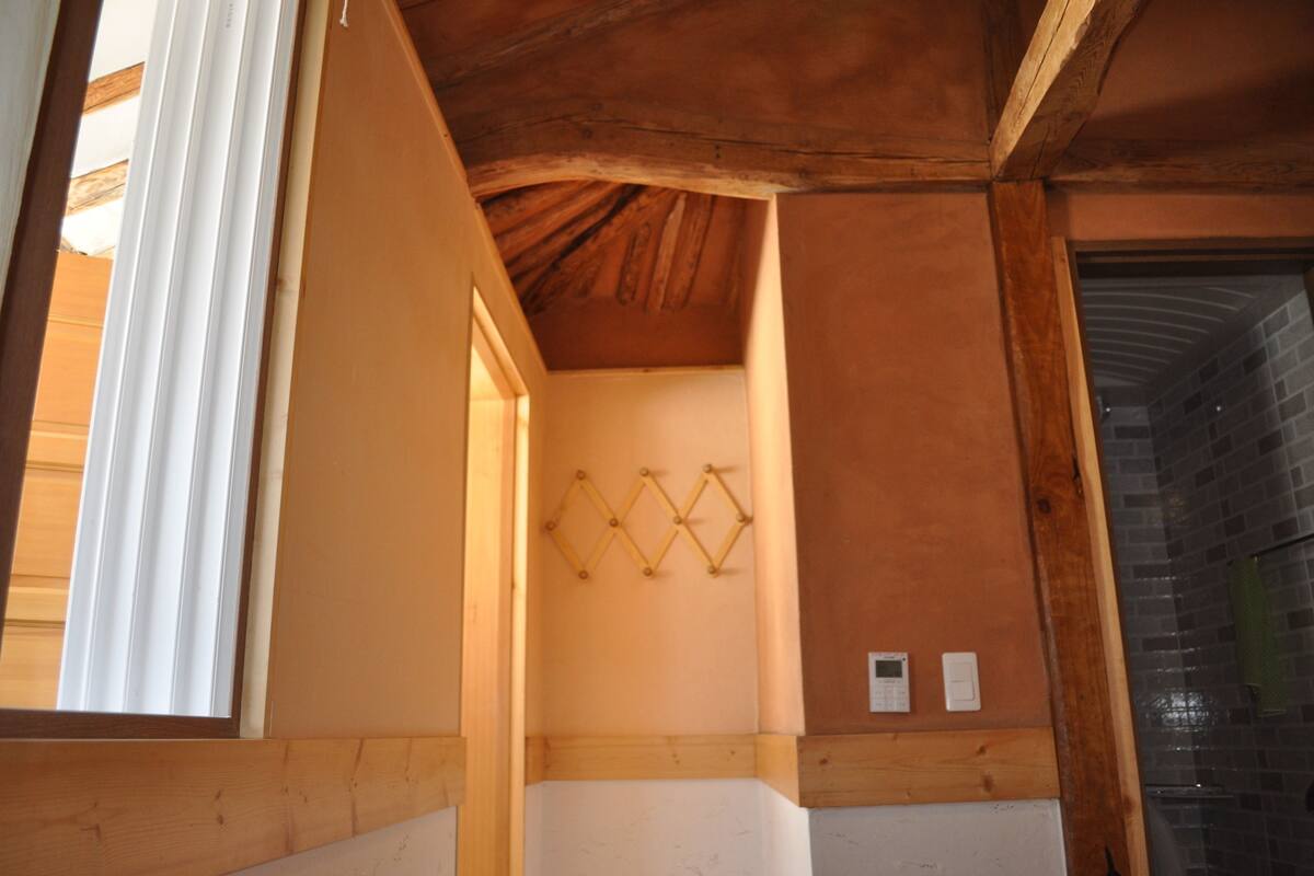 A room with wooden beams on the ceiling, a white door, and a wall-mounted light fixture.