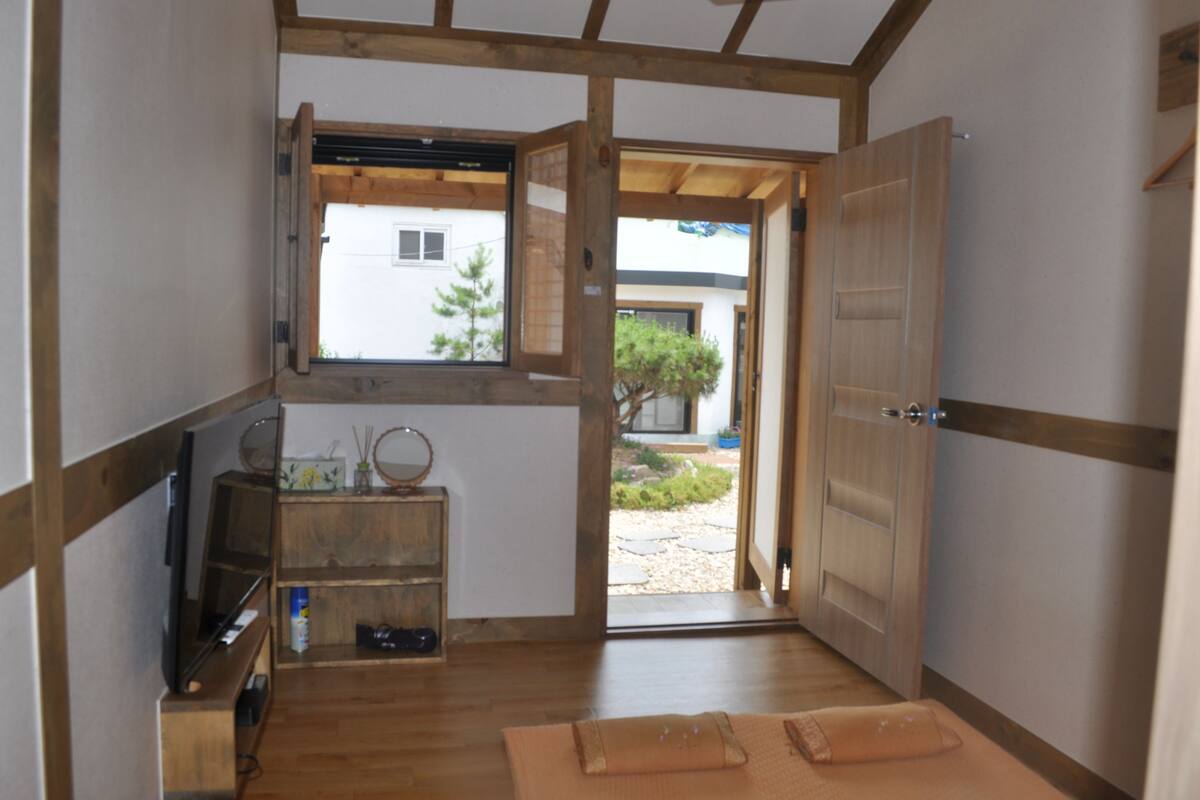 A traditional Japanese room with tatami flooring, a sliding door, a small window, and a wooden shelf with items.