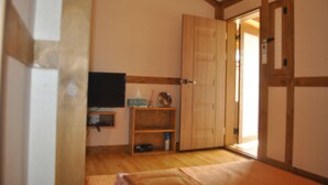 A room with a wooden floor, a television mounted on the wall, a wooden door, and a small shelf with items. - Tosarang Guesthouse (Jeonju)