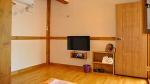 A room with wooden walls and floor, a television on a shelf, a door, and a small shelf with towels. - Tosarang Guesthouse (Jeonju)