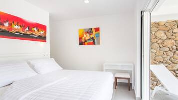 A modern hotel room with a large bed, a small desk, and a stone wall.
