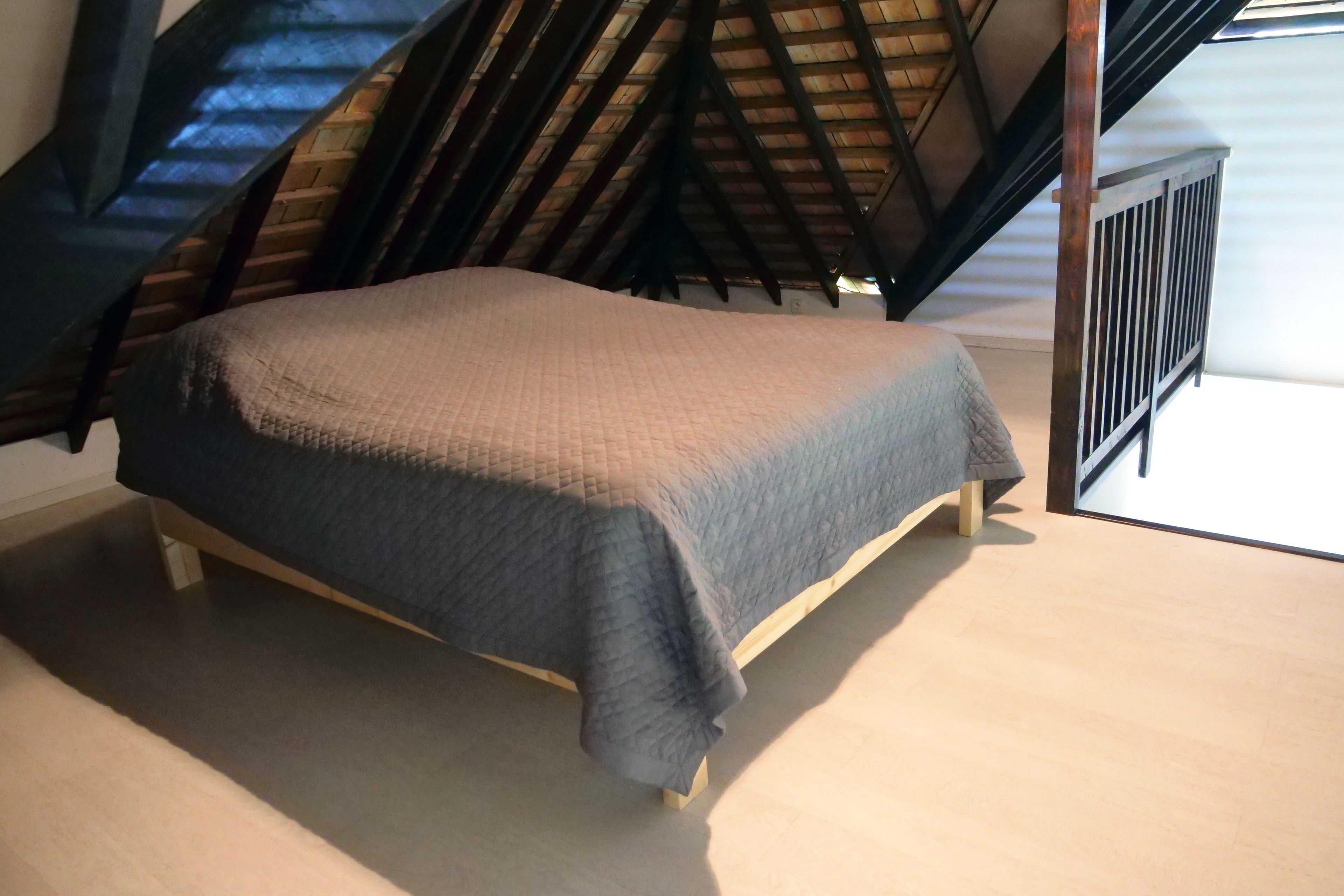 Un dormitorio con cama en una habitación estilo loft, con techo inclinado y vistas a una escalera.