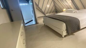 Habitación moderna y compacta con cama, mesita de noche pequeña y ventilador de techo.