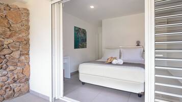 Un dormitorio con pared de piedra, una cama con ropa de cama blanca, un cuadro y una mesita de noche.