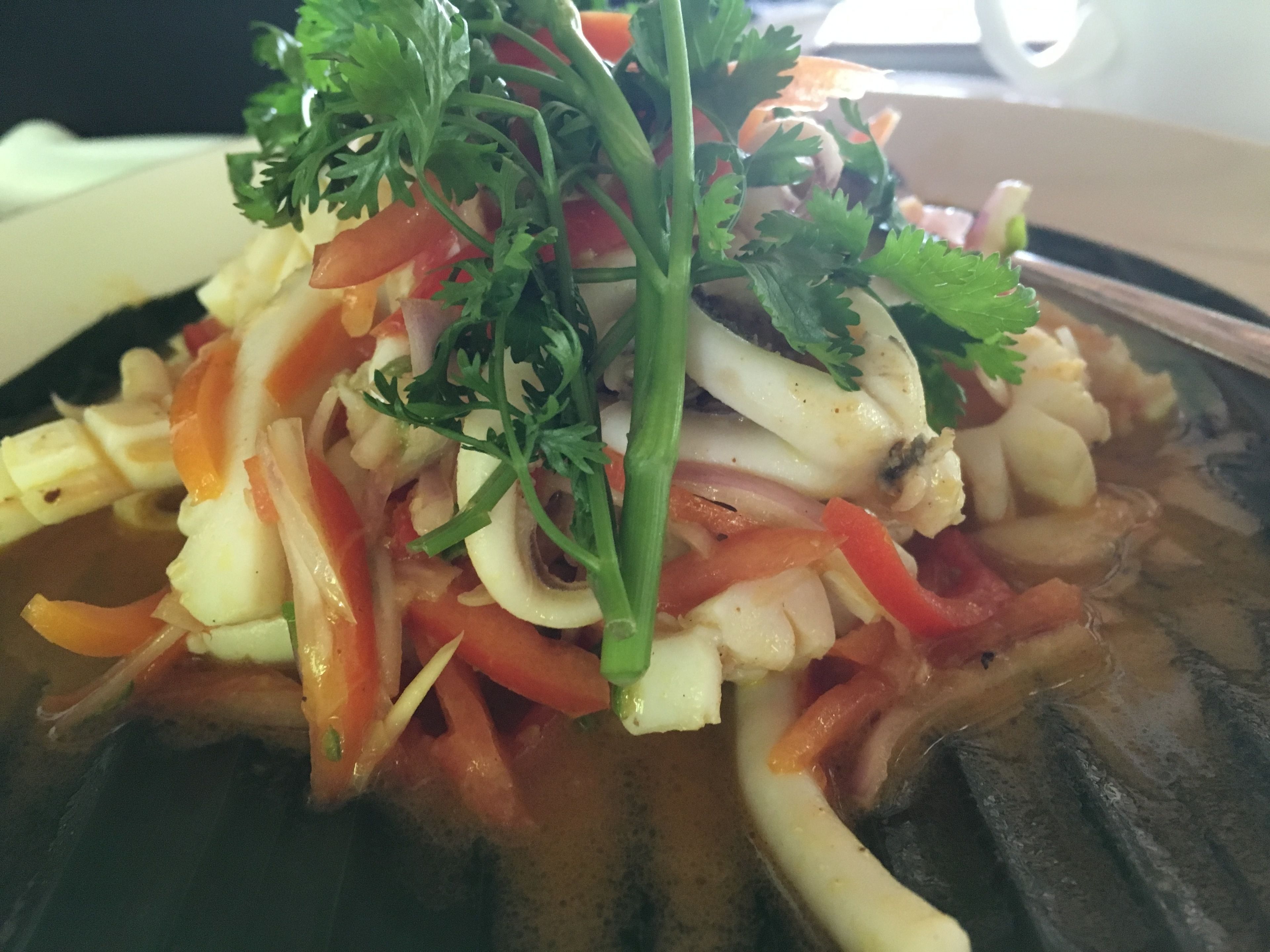 Primer plano de un plato de mariscos con diversas verduras y hierbas.