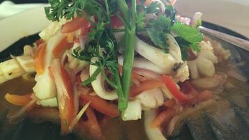 Primer plano de un plato de mariscos con diversas verduras y hierbas.