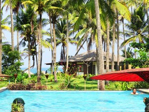 A pool surrounded by palm trees and a thatched-roof building.