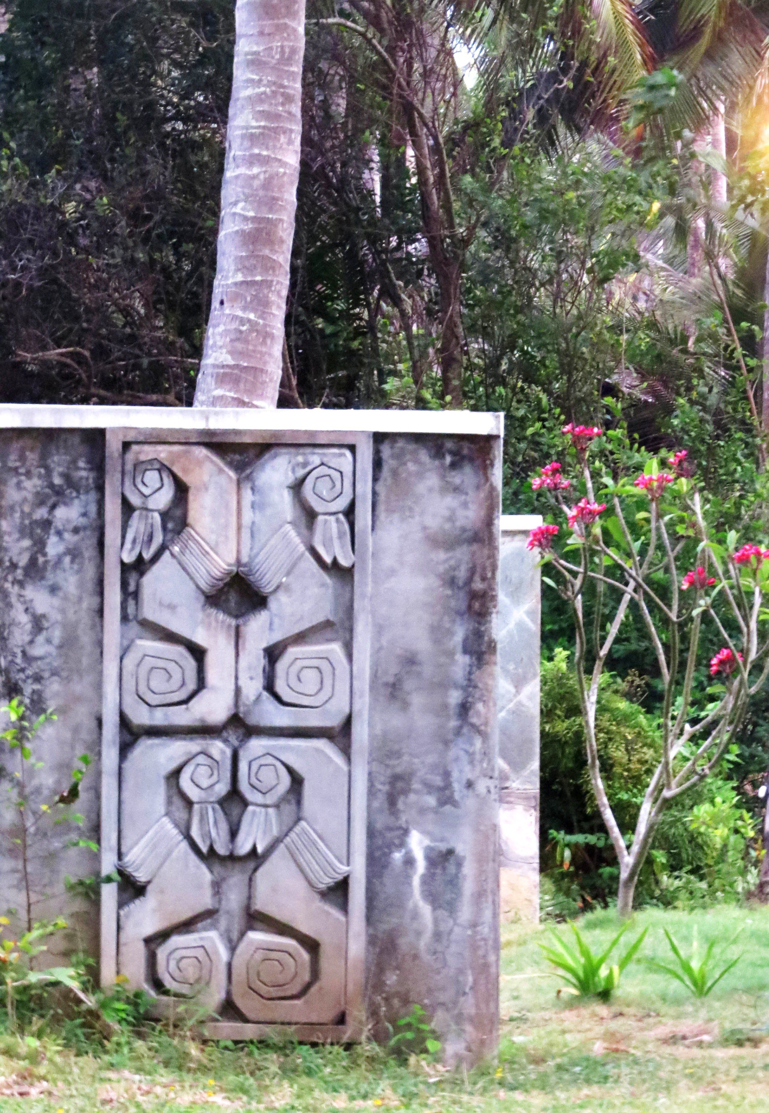 A stone wall with intricate carvings, a palm tree, and a flowering plant.