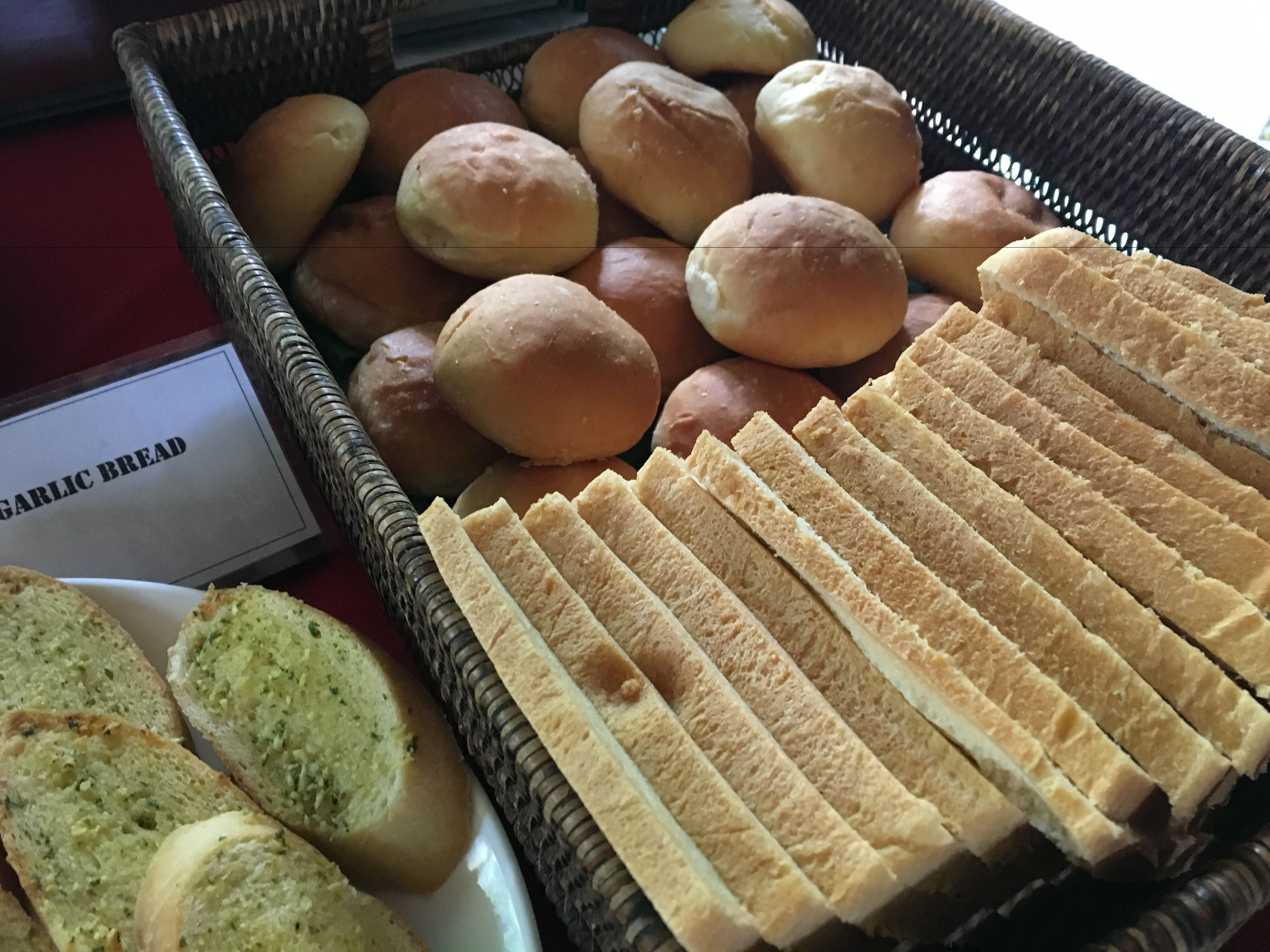 Een mand met diverse broden, waaronder knoflookbrood, stokbroden en broodjes.