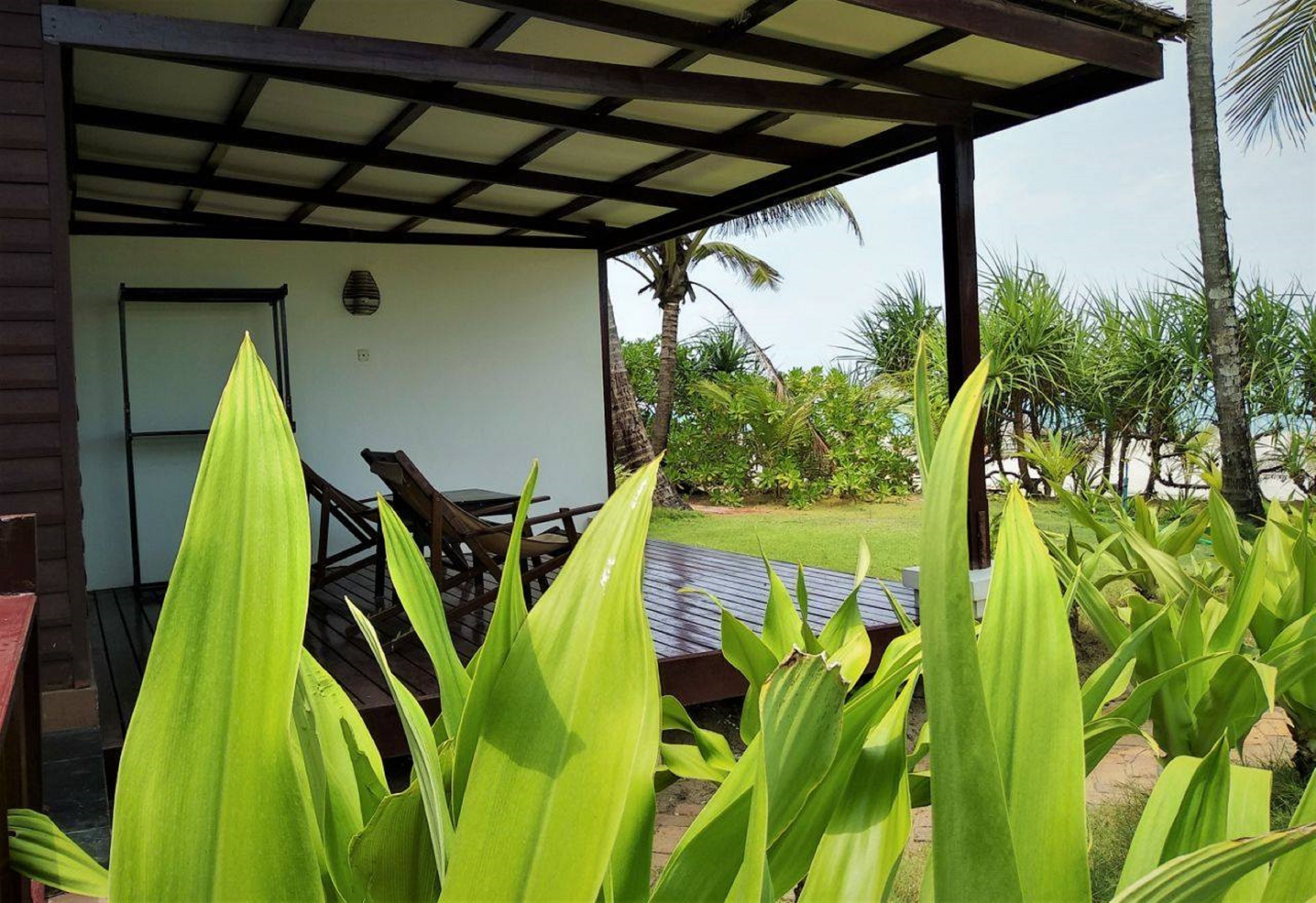A covered outdoor seating area with a table and chairs, surrounded by lush greenery and palm trees.