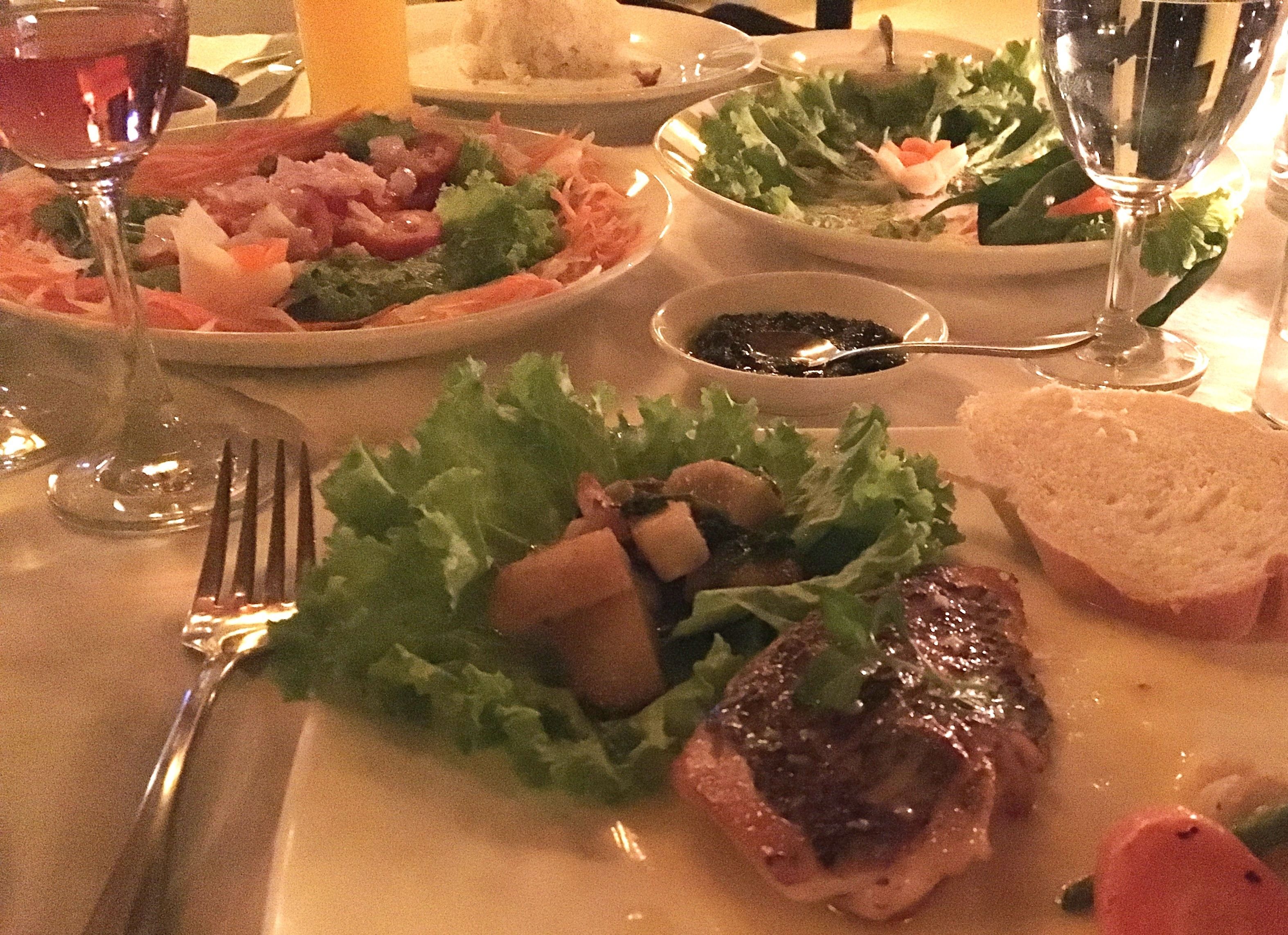 A dining table with plates of food, a fork, and a wine glass.