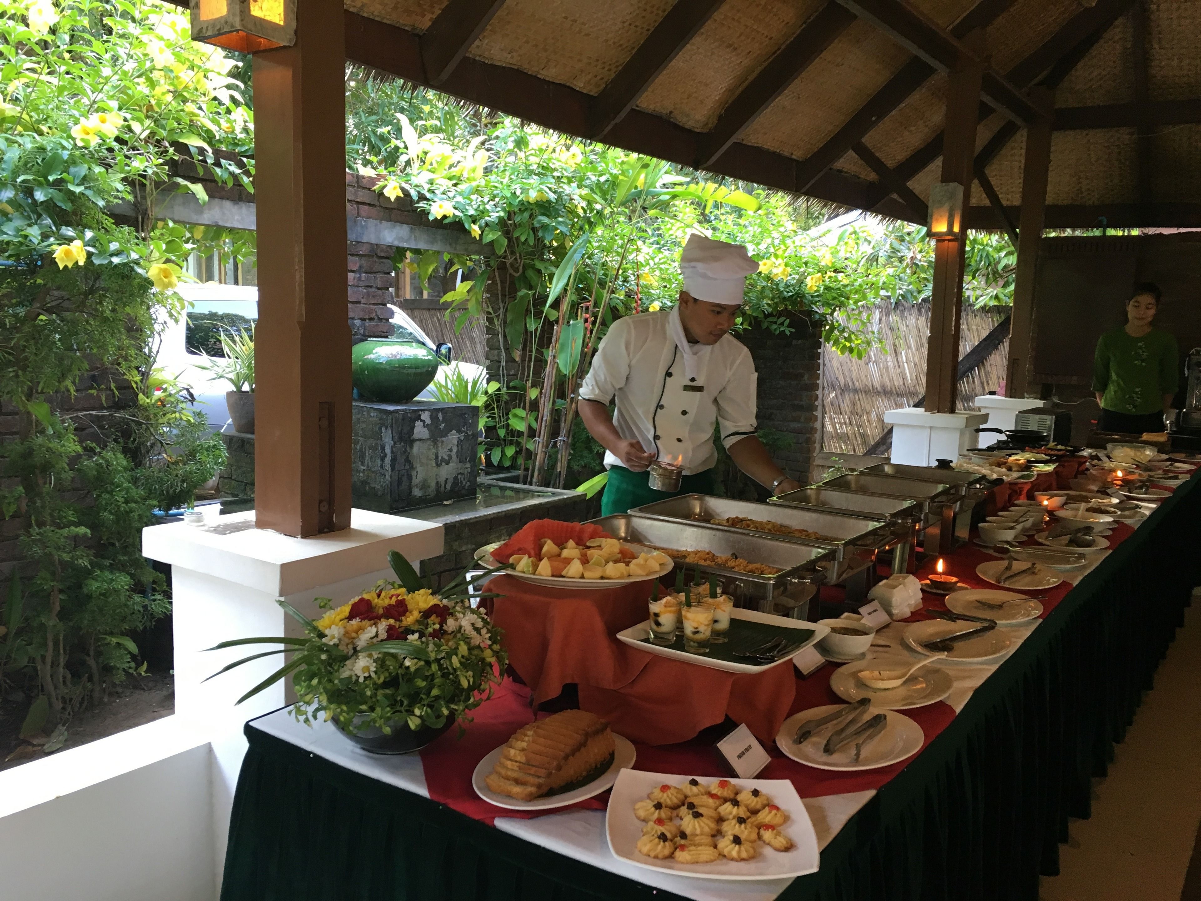 Montaje de bufé con diversos alimentos y un cocinero preparándolos.