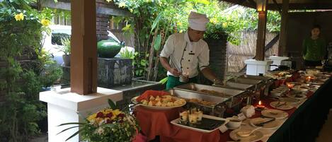 Montaje de bufé con diversos alimentos y un cocinero preparándolos.
