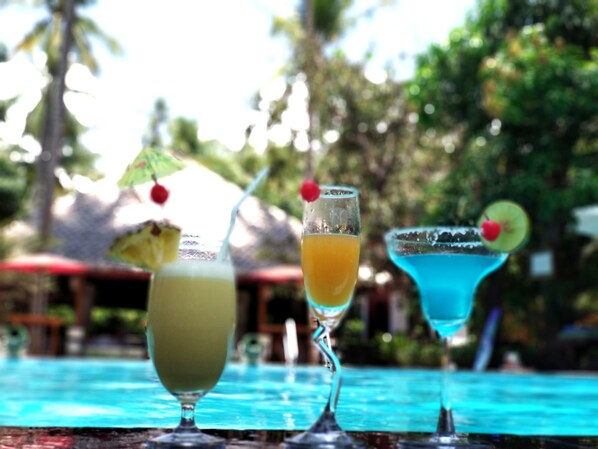 Three cocktails on a table with a pool in the background.