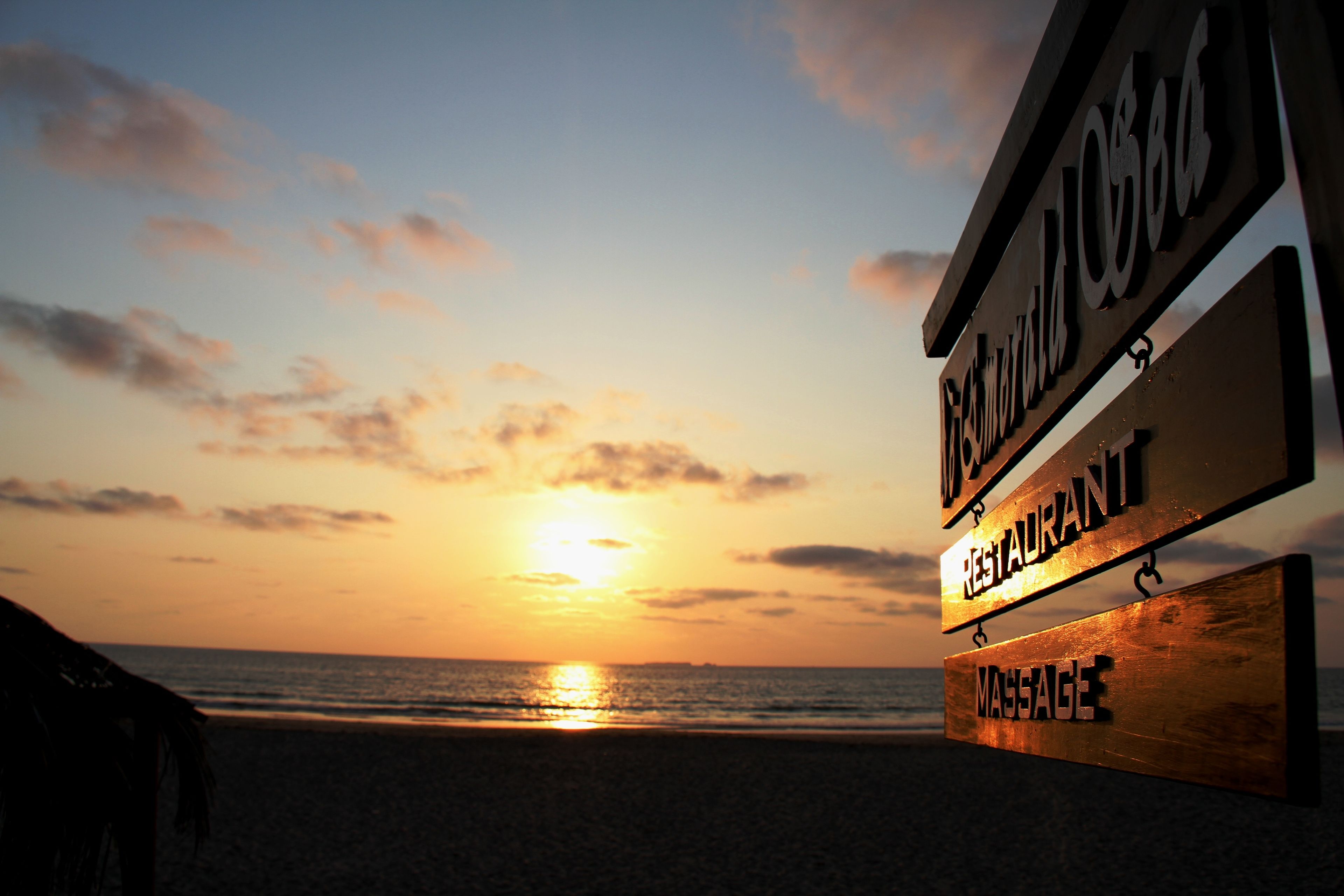 A beach view with a sunset, a sign for a restaurant, and a sign for a massage service.