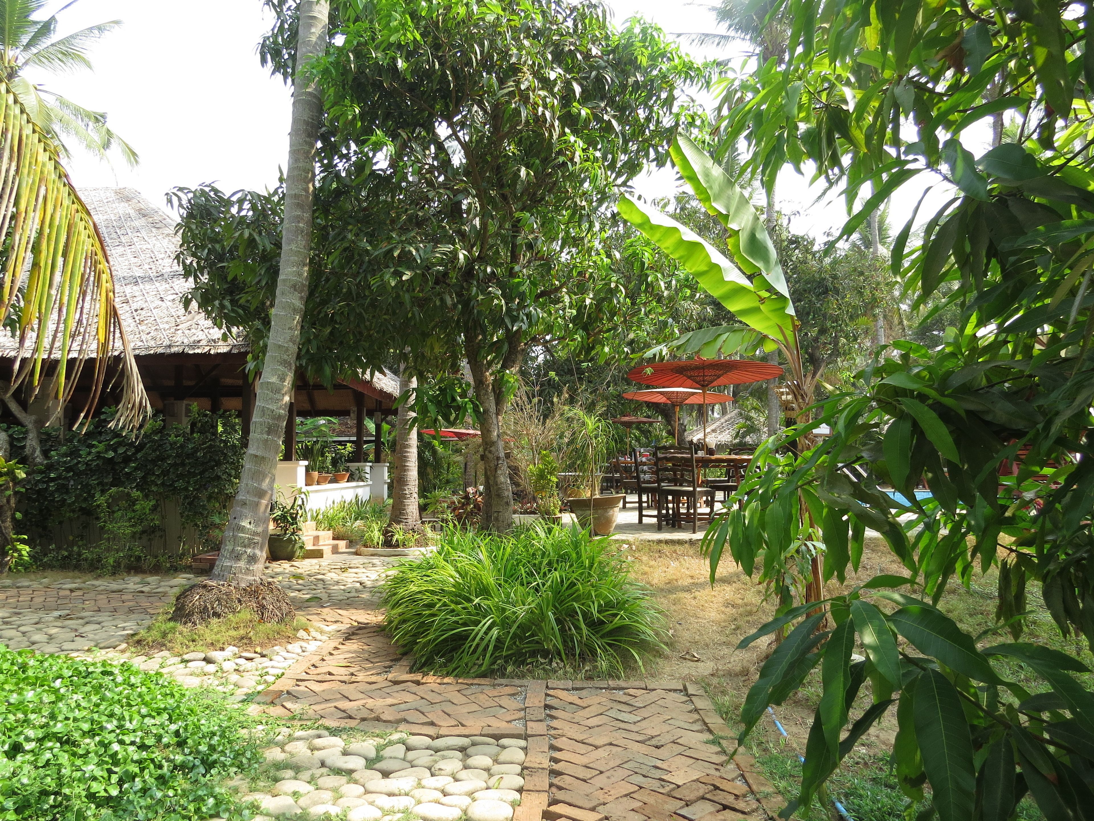 Un jardín con sendero empedrado, mobiliario exterior y abundante vegetación.