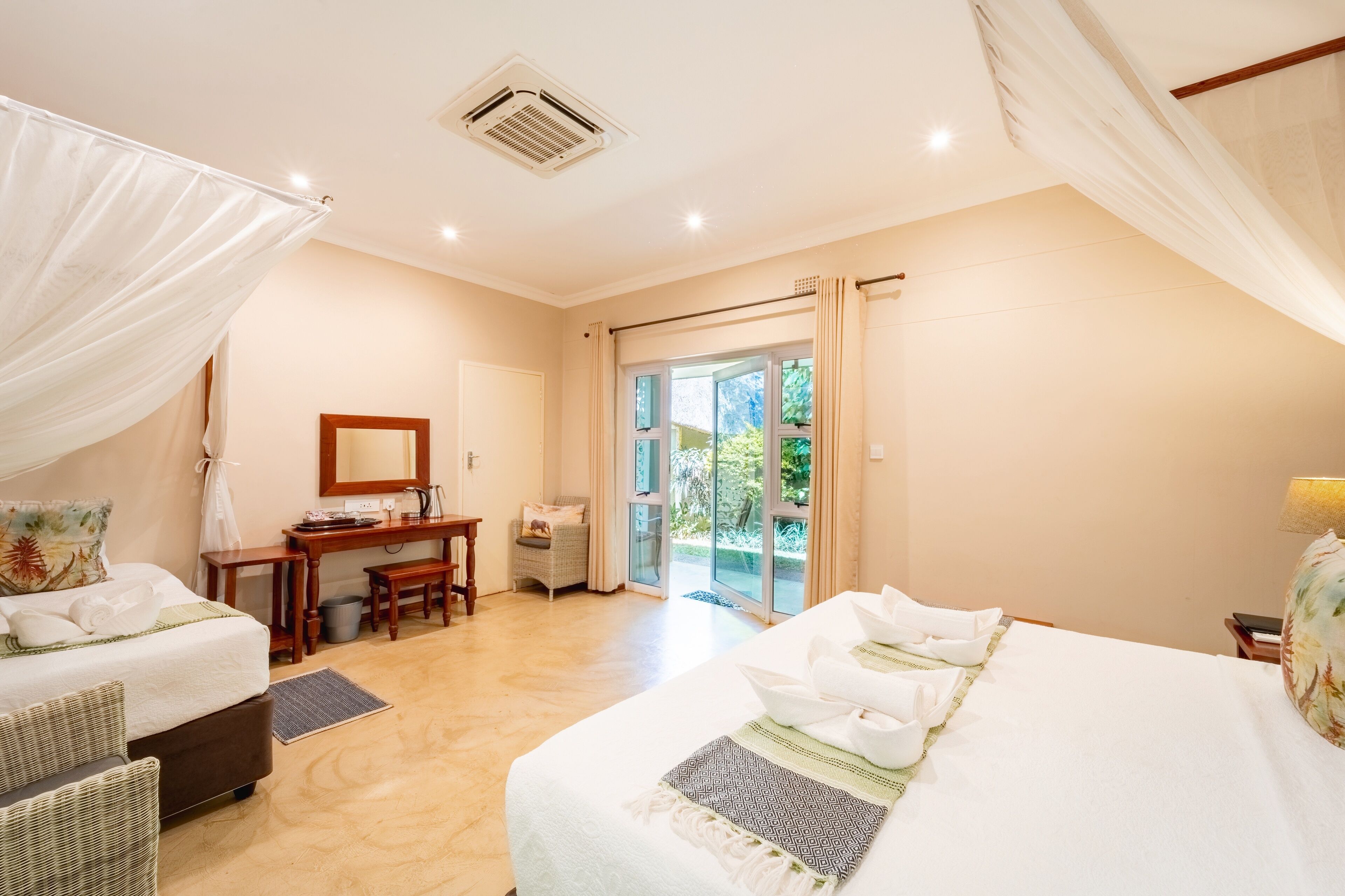 A hotel room with two beds, a desk, a chair, a mirror, and a view of the outdoors.