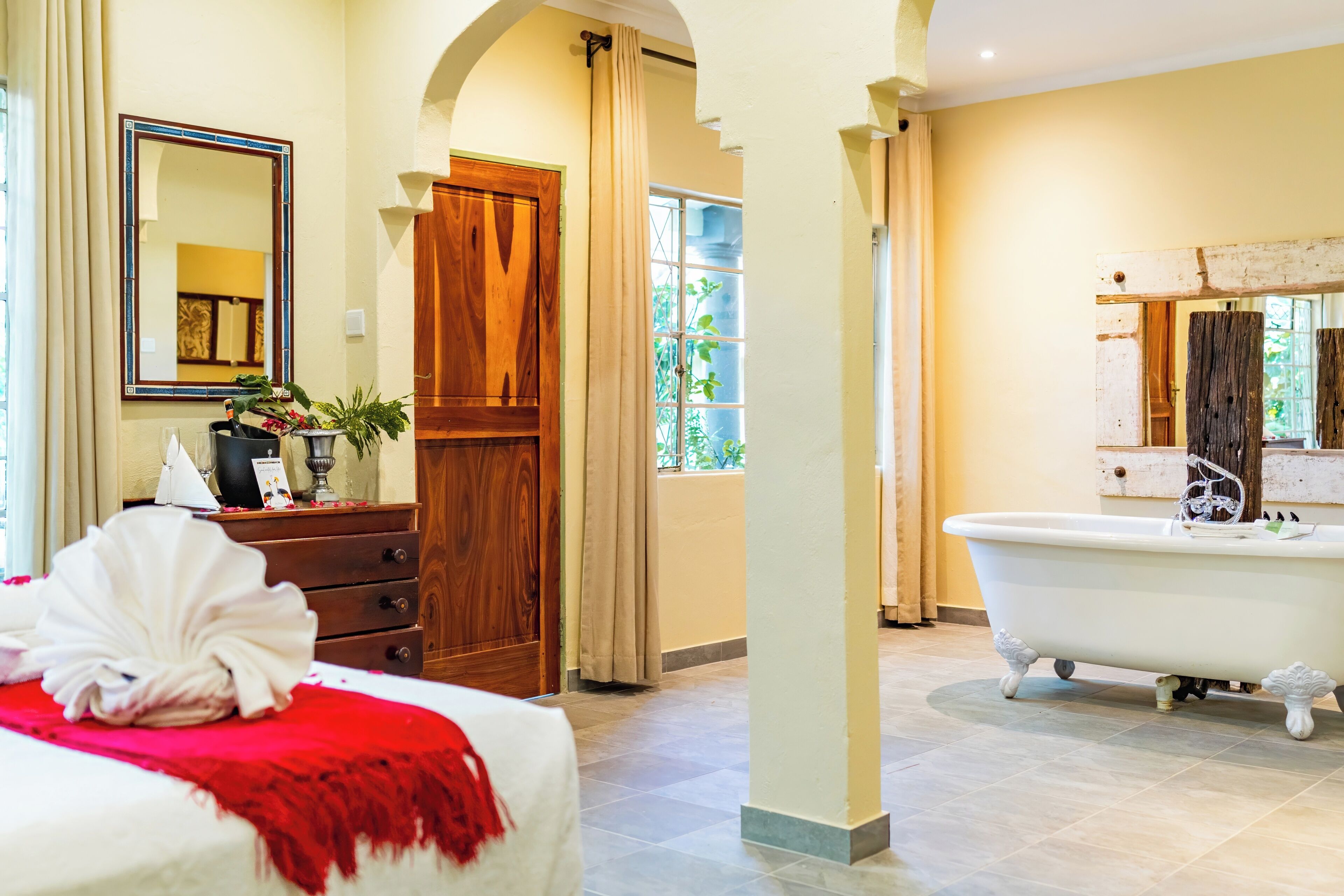 A hotel room with a large bed, a wooden wardrobe, a bathroom with a white bathtub, and a large mirror.