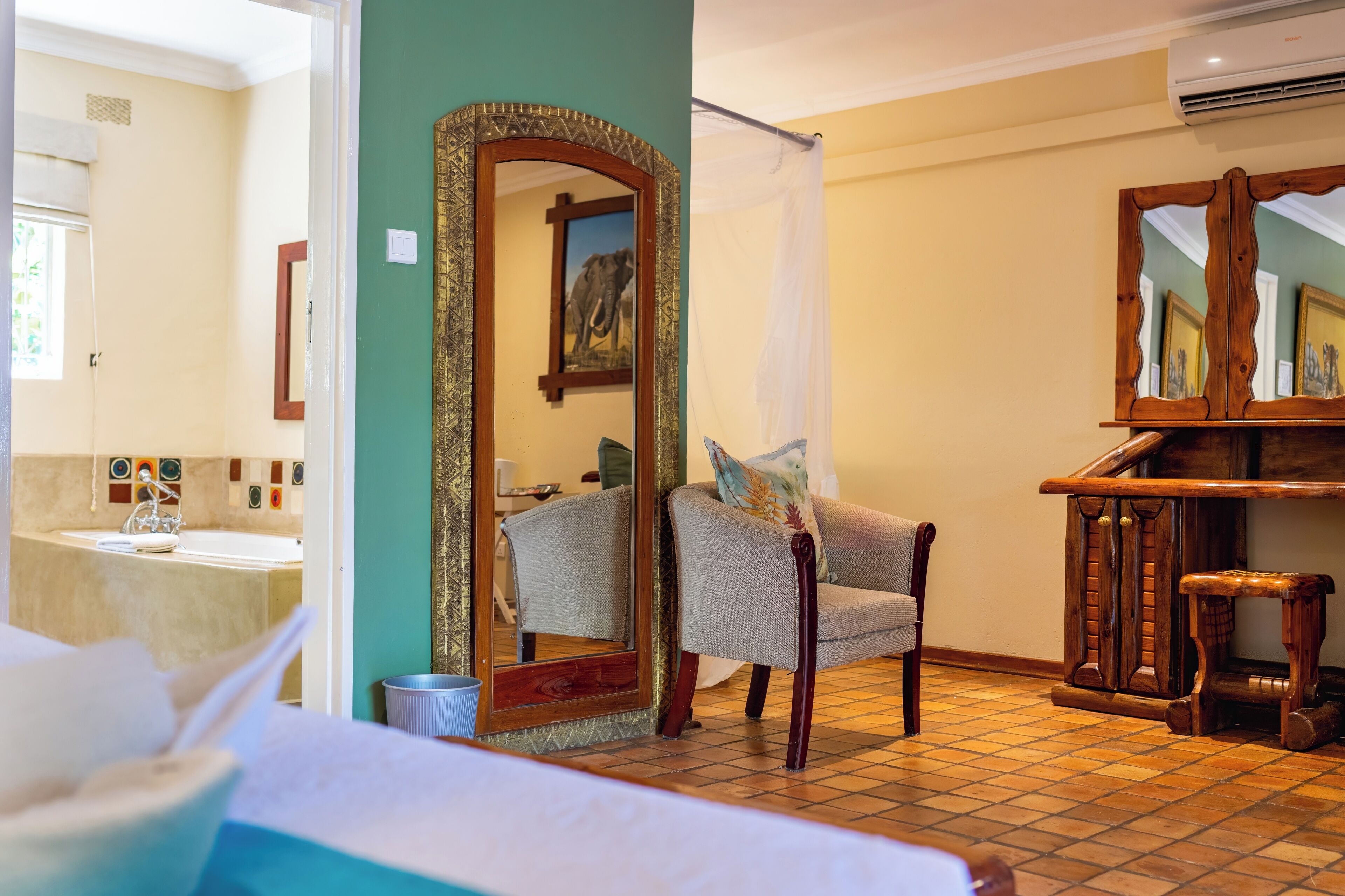 A hotel room with a large mirror, a chair, a small stool, and a bed.