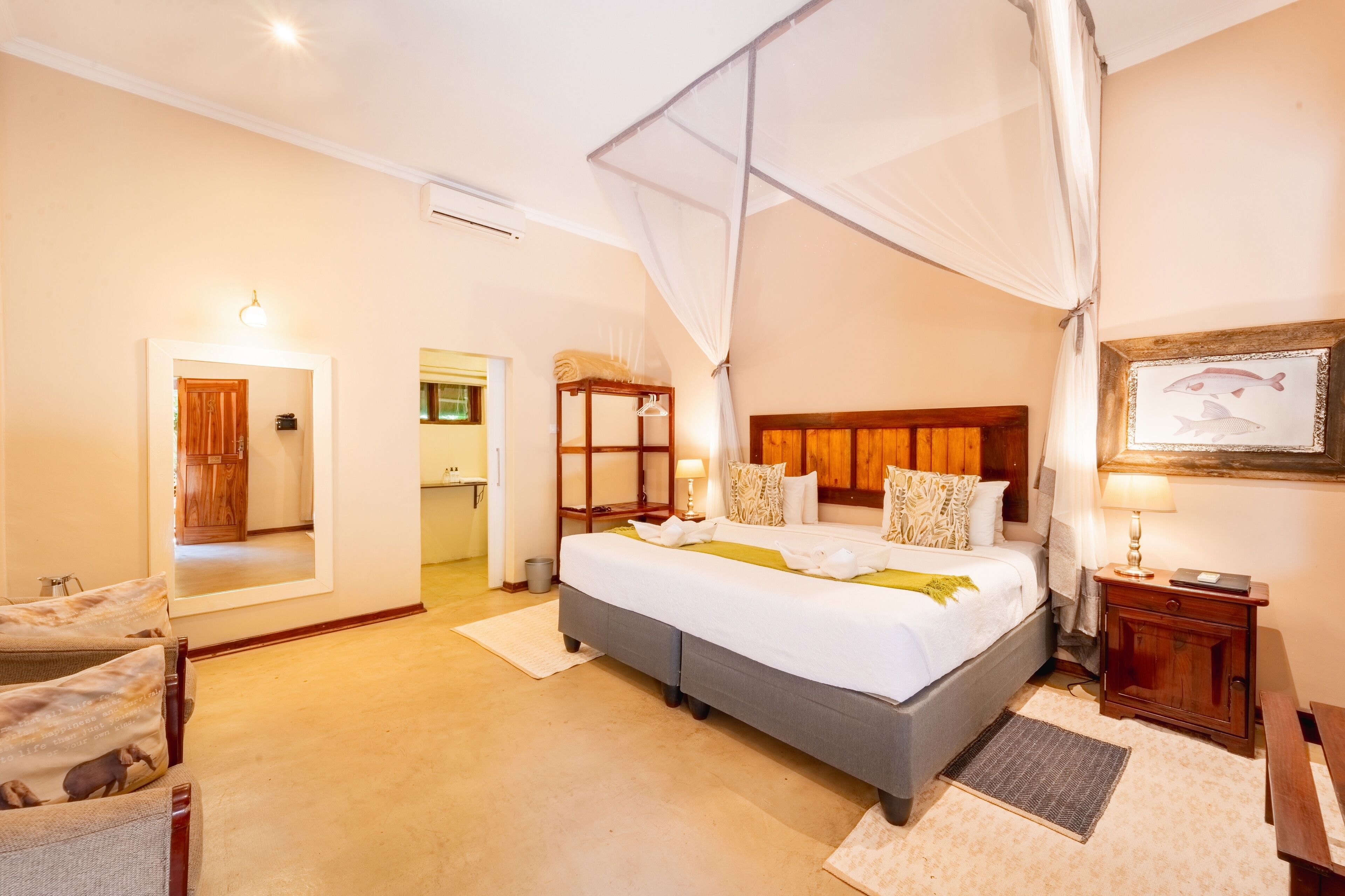 Quarto com cama grande, mesa de cabeceira, criado-mudo, espelho, armário de madeira e quadro na parede.