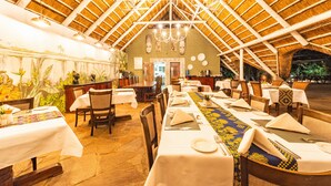 A restaurant with a high, thatched roof and stone flooring, featuring long communal tables set for dining. - Bayete Guest Lodge (Victoria Falls)