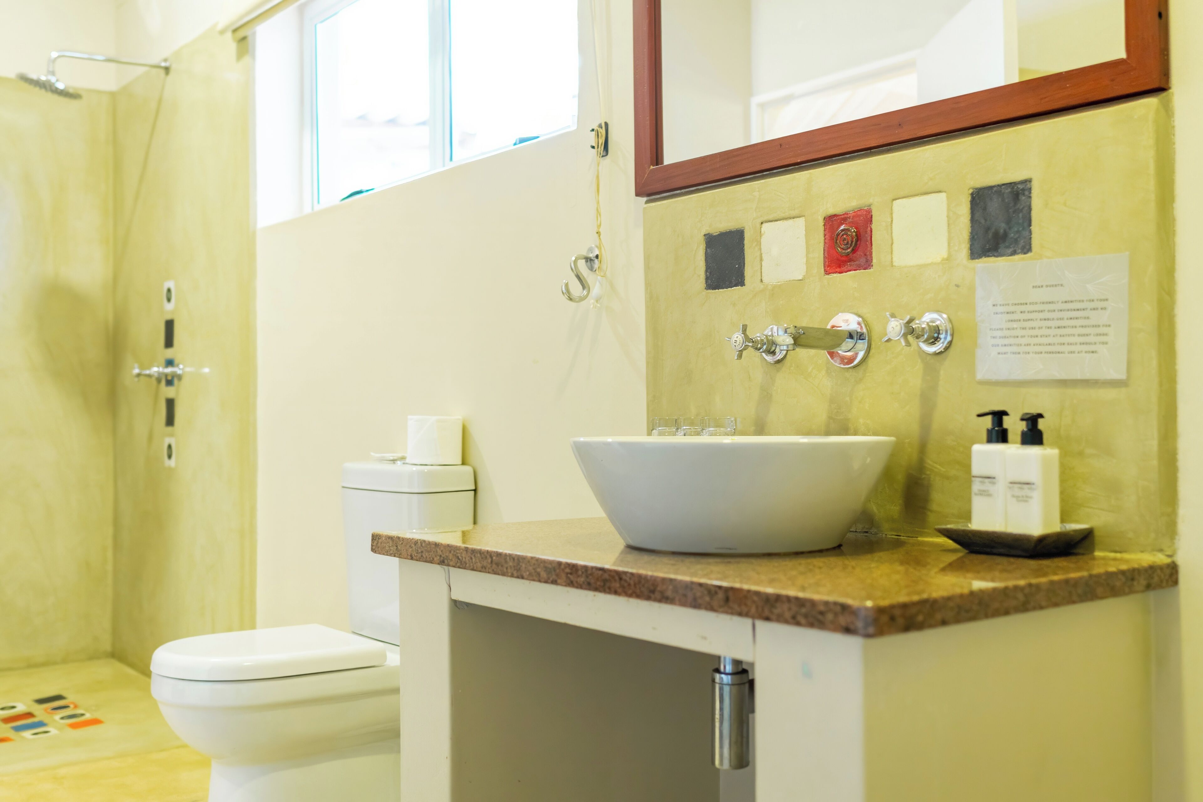 A bathroom with a white sink, a toilet, and a shower. There is a mirror above the sink and a window above the shower.