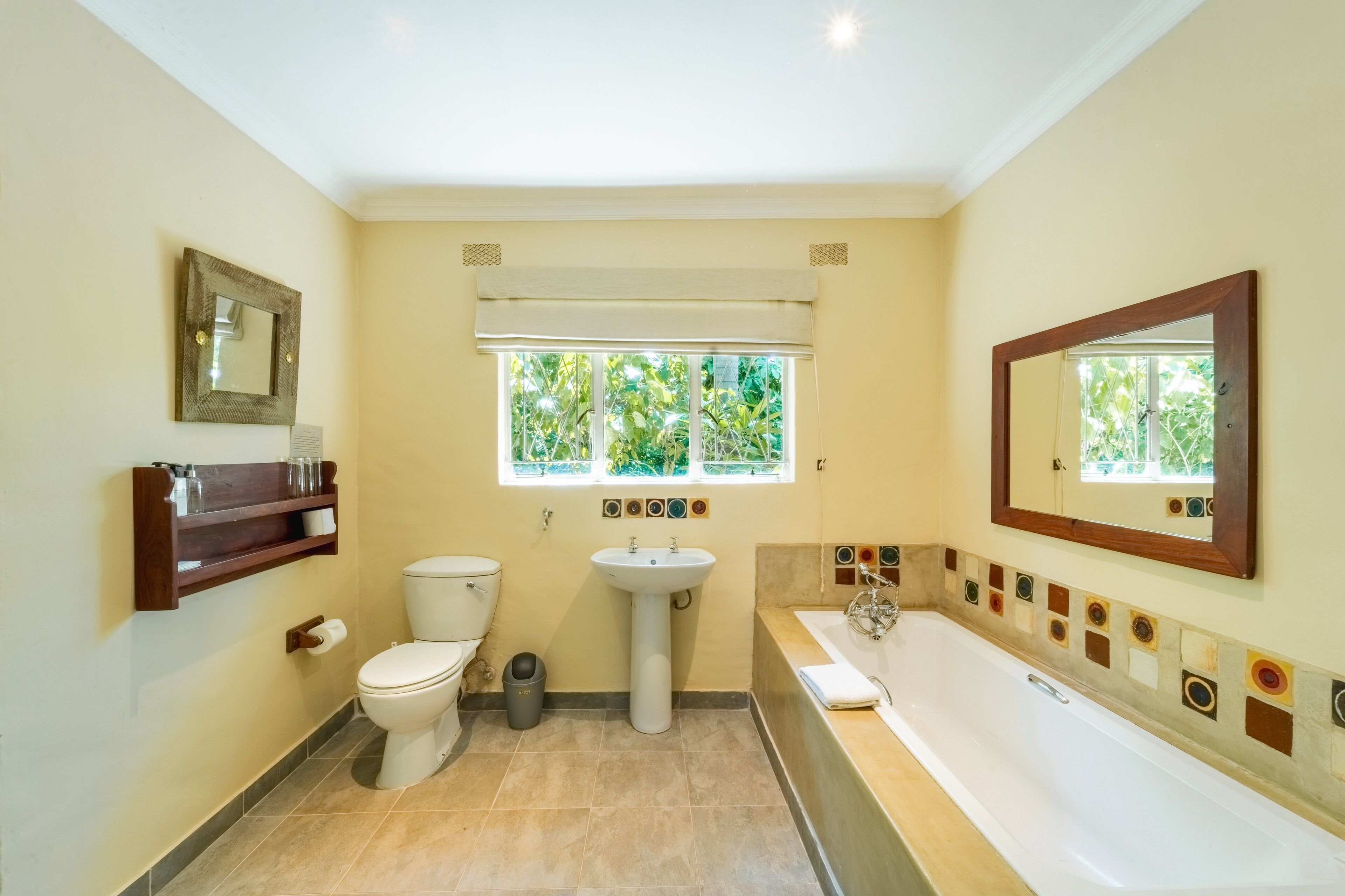 Ein Badezimmer mit Toilette, Waschbecken und Badewanne. Ein Fenster bietet Blick auf grüne Vegetation draußen.