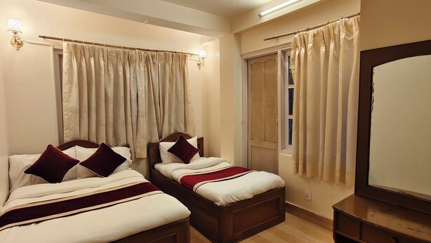 Habitación de hotel con dos camas, un espejo grande y una ventana con cortinas.