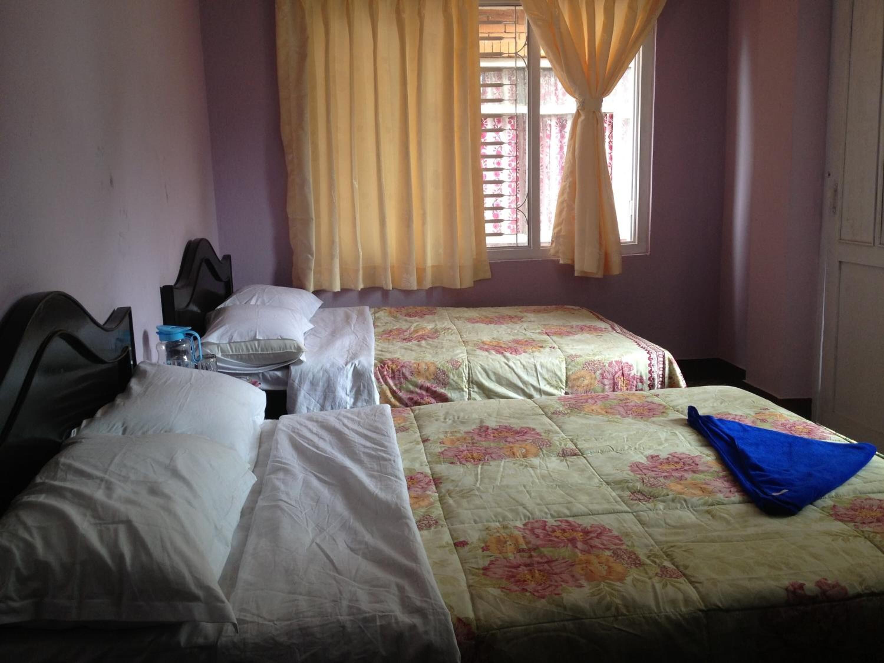 Une chambre avec deux lits, une fenêtre avec des rideaux et une table de chevet avec une lampe.