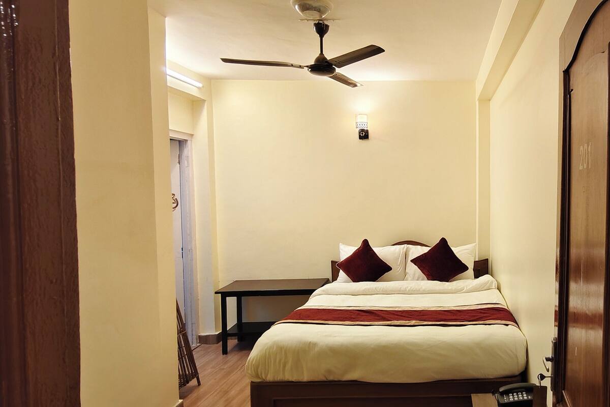 A hotel room with a bed, a ceiling fan, a bedside table, and a door.