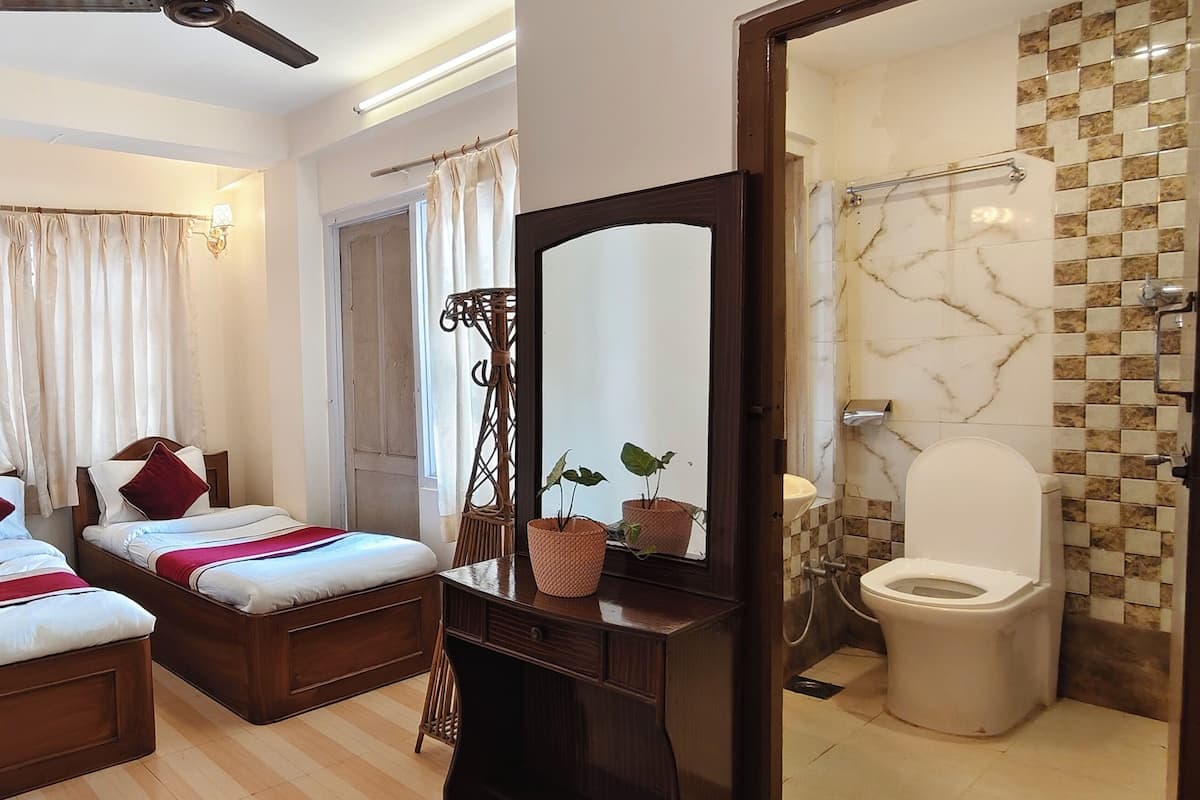 A hotel room with two beds, a bathroom with a marble-tiled shower, and a wooden dresser.
