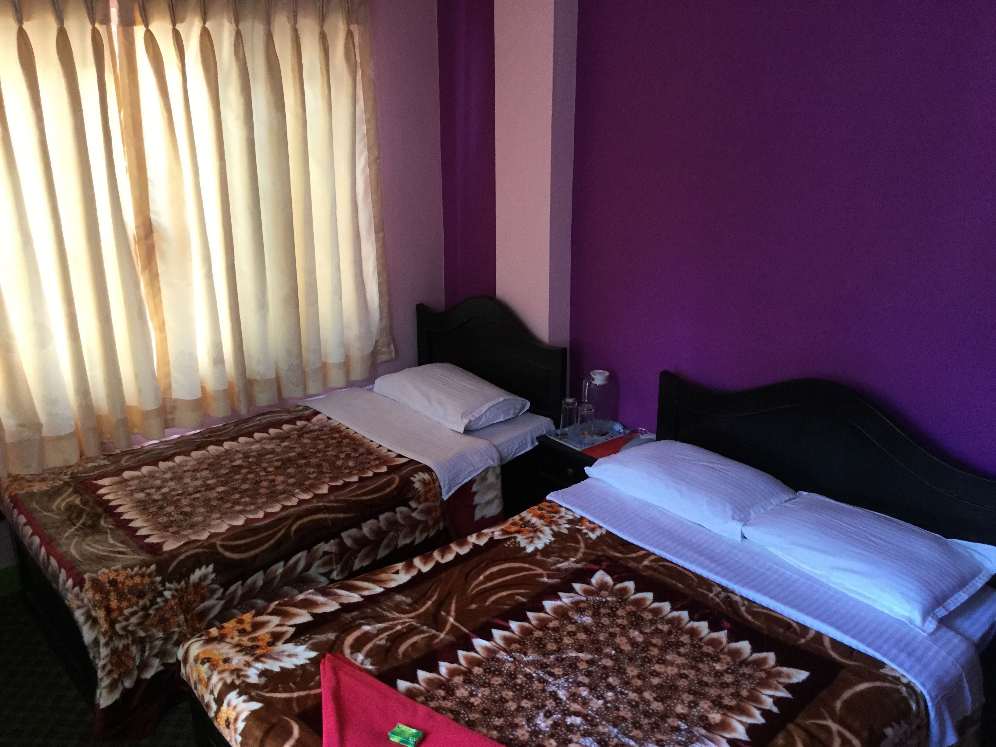Une chambre avec deux lits, une fenêtre avec des rideaux et un mur violet.