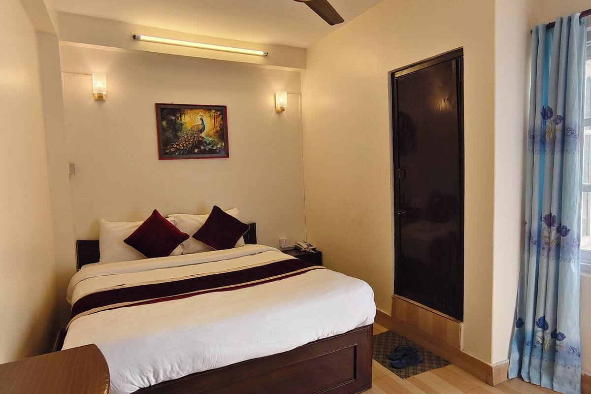 A hotel room with a bed, a mirror, a painting, a door, and a window with curtains.